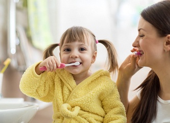 A little girl brushing her teeth with her mom