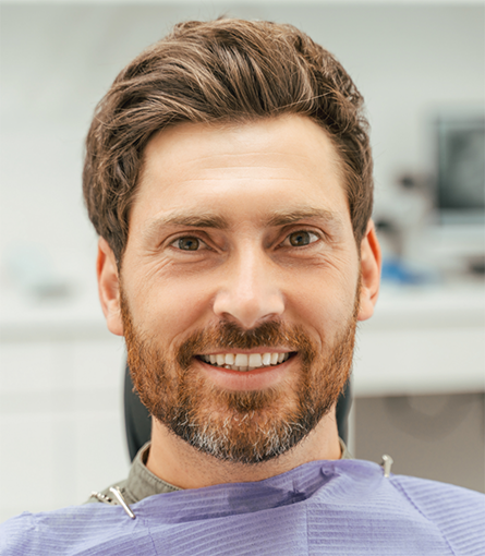Man with beard sitting in dental chair and smiling