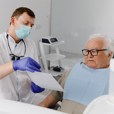Dentist with mask showing piece of paper to male patient