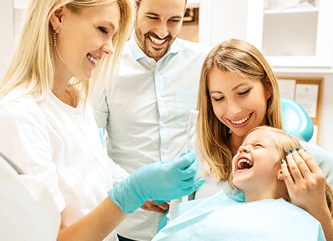 A young girl in the dentist chair with her parents and the dentist