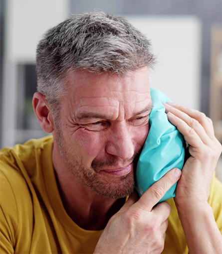 Man holding cold compress against his cheek