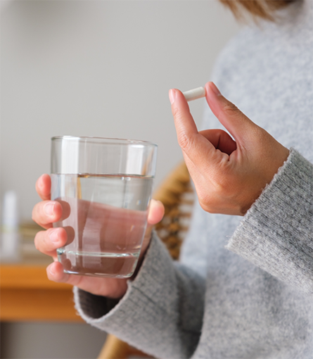 Hand holding a glass of water and a pill
