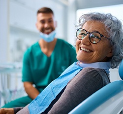 Woman with black glasses smiling while sitting in treatment chair
