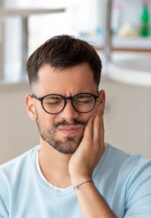 a man holding his cheek due to tooth pain