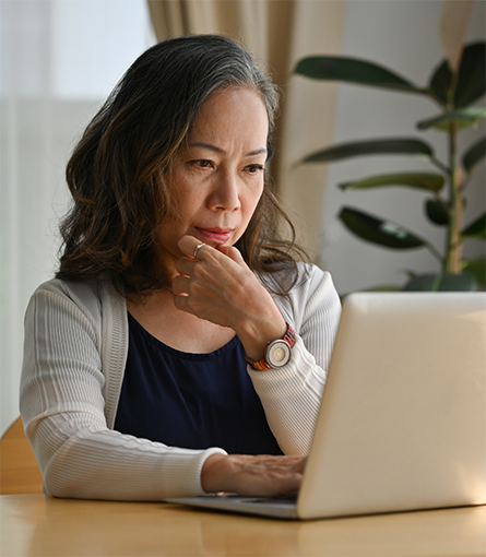 Woman sitting at table and looking thoughtfully at laptop