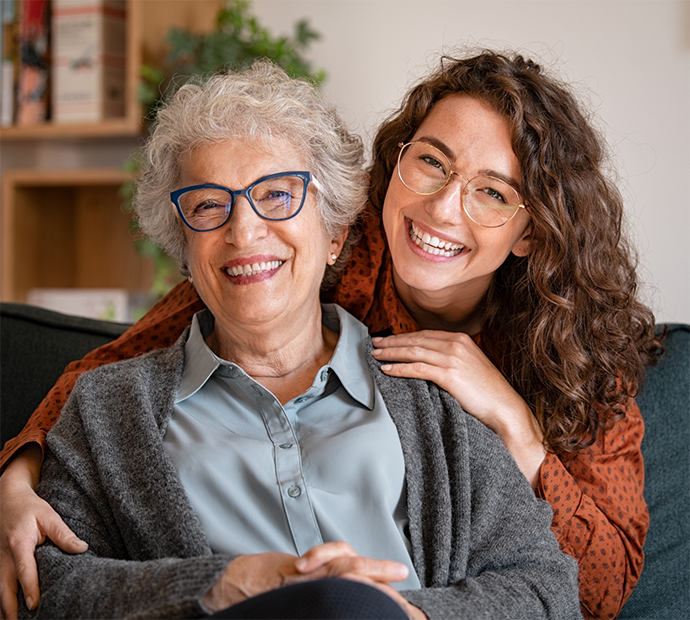 Older woman with glasses being hugged from behind by younger woman with glasses