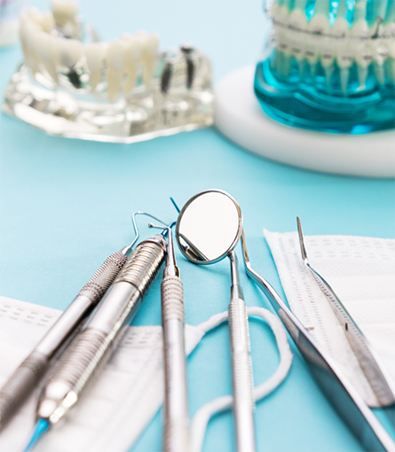 Dental instruments lying on blue surface with models of teeth sitting nearby