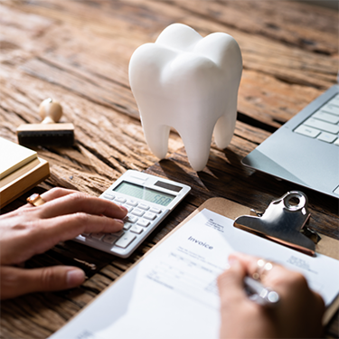 Using calculator and filling out form on clipboard with tooth shaped paperweight sitting nearby