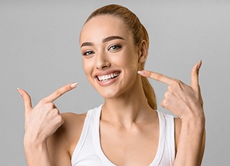 young woman pointing to smile after getting veneers in Dix Hills