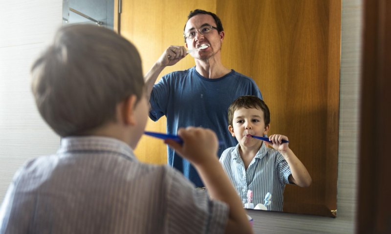 A father and son brushing their teeth together.