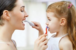 Mother and young daughter brush each other's teeth