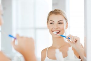 Woman looking in mirror while brushing her teeth at dentist in Dix Hills.