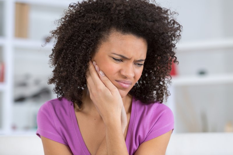 person with toothache who needs emergency dental visit holding cheek